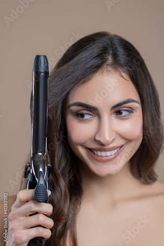 Joyful woman with curling iron on her hair