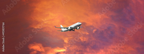 Ultra wide panoramic zoom photo of passenger airplane taking off at sunset with beautiful orange sky and clouds