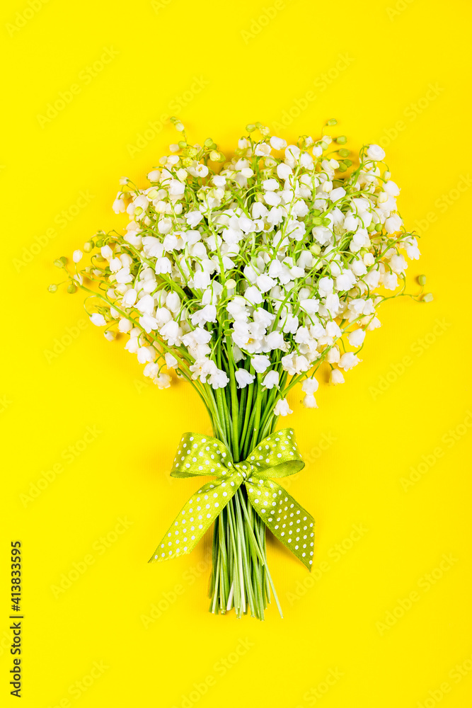 bouquet of lily of the valley flowers with a green bow on a yellow background top view close up