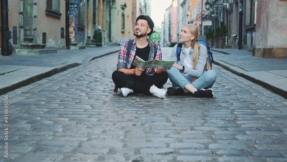 Tourists couple with map sitting on pavement and admiring historical surroundings. They are excited and smiled. Tourists couple with map sitting on pavement and admiring historical surroundings. They are excited and smiled.