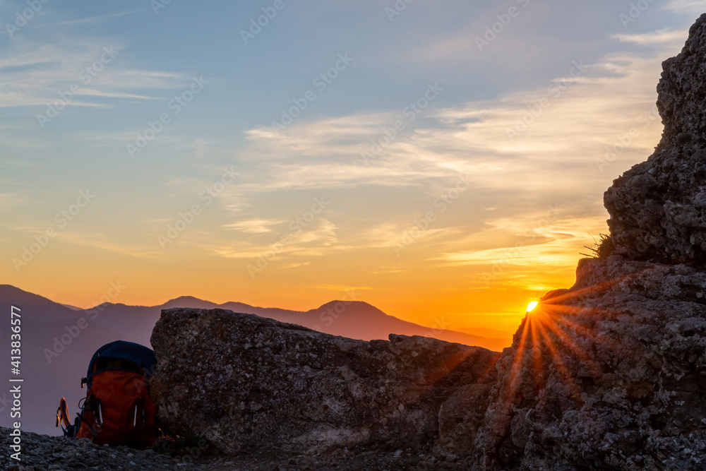 The rays of the setting sun make their way through a piece of rock and a traveler's backpack