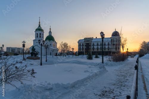 Dawn in the city of Tobolsk (Siberia, Russia) in winter. The sun that appeared from behind the horizon illuminated one of the squares with many lanterns, trees and houses. Cold morning with light fog 