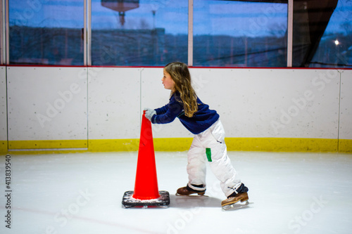 A little girl in snow pants and ice skates skates alone in an ice rink photo