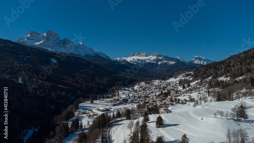 Aerial drone view of valley around Cortina d'Ampezzo, looking from the village of Volo di Cadore towards the snowy hills in february on a sunny day.