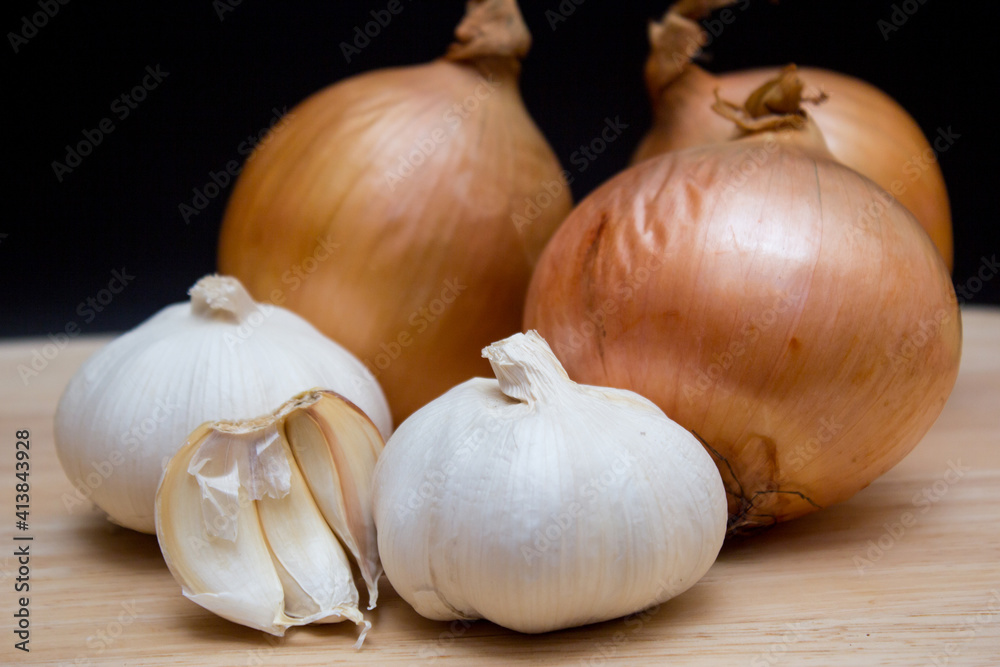 Fototapeta premium The yellow onions and garlics isolated black background on a wooden cutting board