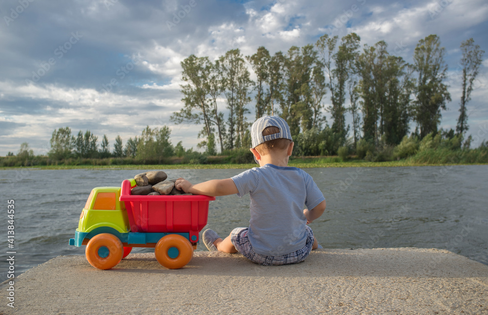 Two year old boy playing at riverside with dump truck Two year old boy playing at riverside with dump truck