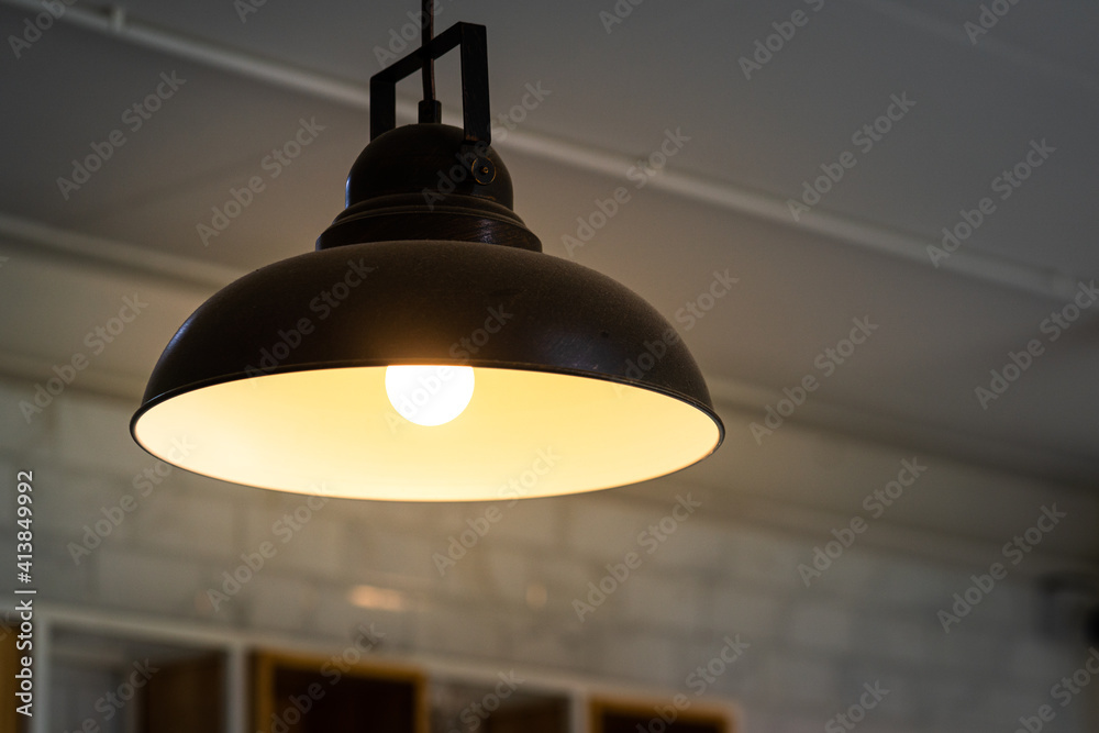 A ceiling loft style electrical lighting lamp with warm light bulb glowing. It's use to decorate in luxury cafe or restaurant. Interior decor object photo, selective focus at the bulb.