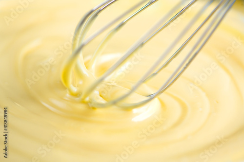White Chocolate mixing with a whisk. Pouring melted liquid premium milk white chocolate. Close up of molten liquid hot chocolate swirl. Confectionery. Confectioner prepares dessert, icing 