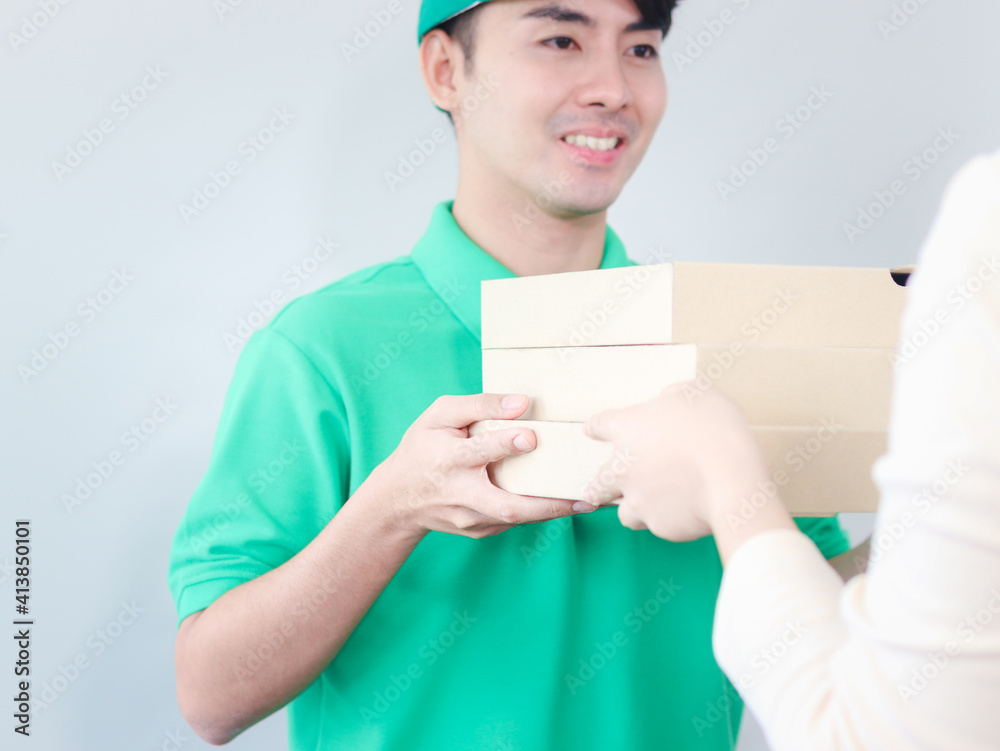 Smiling young Asian delivery man in green T-shirt uniform holding pizza boxes and giving goods to customer hands, tracking, shipping and courier delivery services express concept. Smiling young Asian delivery man in green T-shirt uniform holding pizza boxes and giving goods to customer hands, tracking, shipping and courier delivery services express concept.