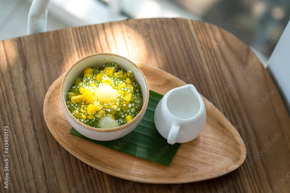 Sago or Saku topping with corn, longan fruits and coconut milk, served in white bowl on the wooden plate. This is one of famous tradition Thai dessert food. Sweet food close-up photo. Sago or Saku topping with corn, longan fruits and coconut milk, served in white bowl on the wooden plate. This is one of famous tradition Thai dessert food. Sweet food close-up photo.