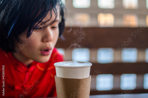 A small child sits at a cafe table blowing on a steamy cup of cocoa