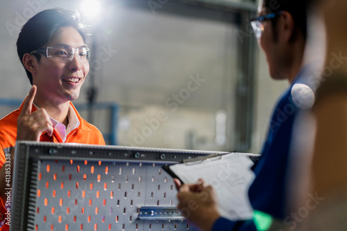 Male Asian engineer professional  having a discussion standing concult cnc machine in the factory ,two asian coworker brainstorm  explaining and solves the process of the cnc operate machine photo