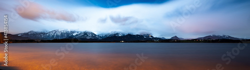 Long exposure panorama of the alps at night with the hopfensee in the foreground