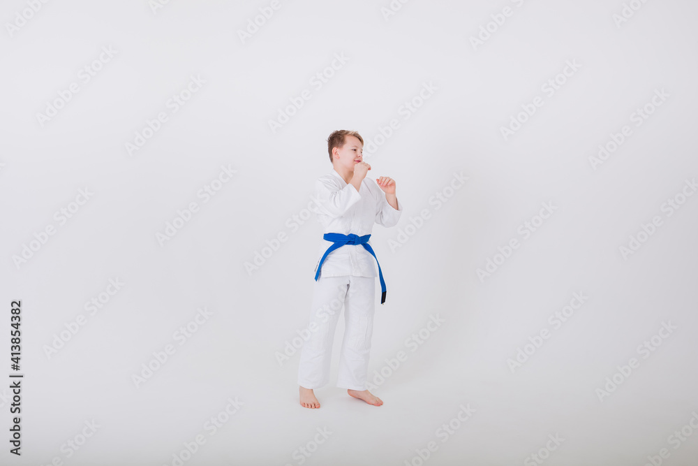 boy in a white kimono with a blue belt stands sideways in a pose on a white background with space for text. Hand-to-hand combat boy in a white kimono with a blue belt stands sideways in a pose on a white background with space for text. Hand-to-hand combat