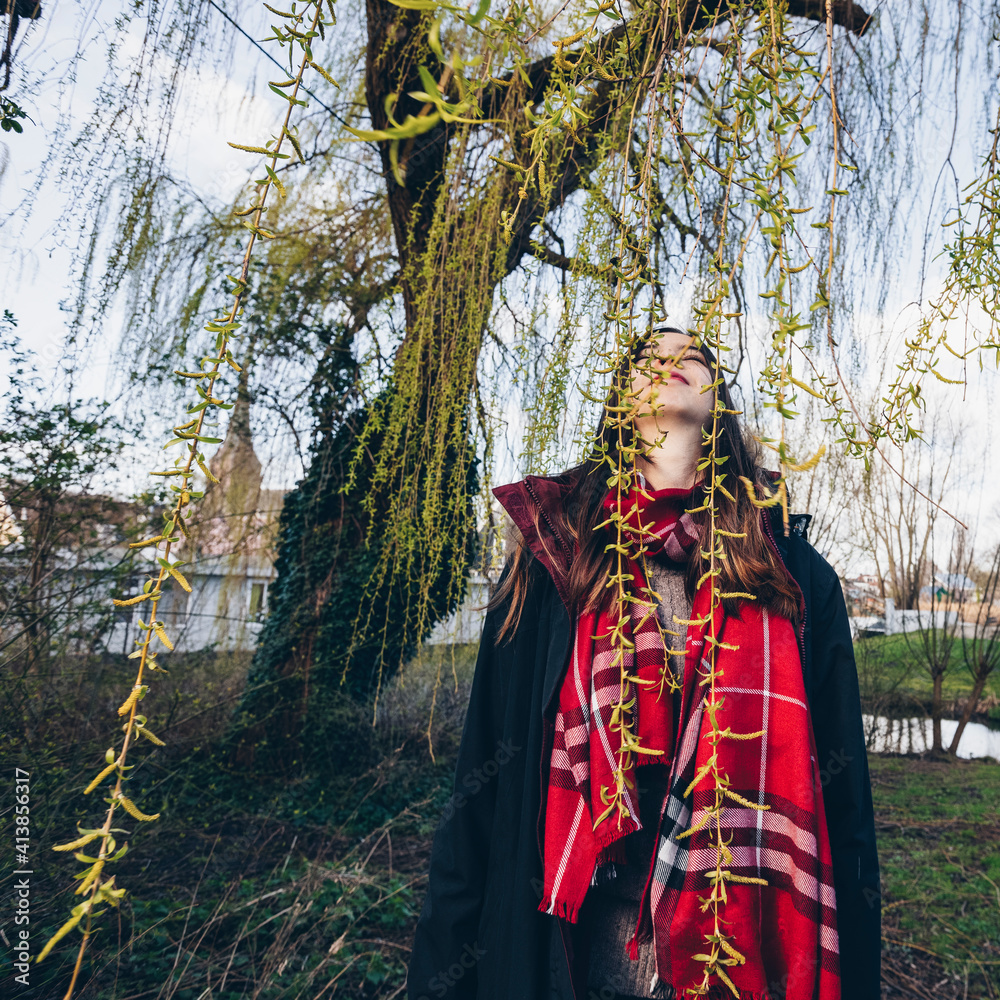 Woman in warm clothes standing under willow in first day of spring. Woman in warm clothes standing under willow in first day of spring.