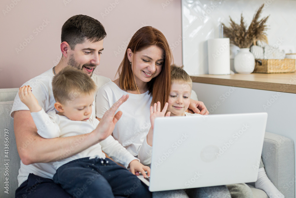 Young family, husband, wife and two young sons, sitting at home in the kitchen, and communicating via video link with family, using laptop Young family, husband, wife and two young sons, sitting at home in the kitchen, and communicating via video link with family, using laptop