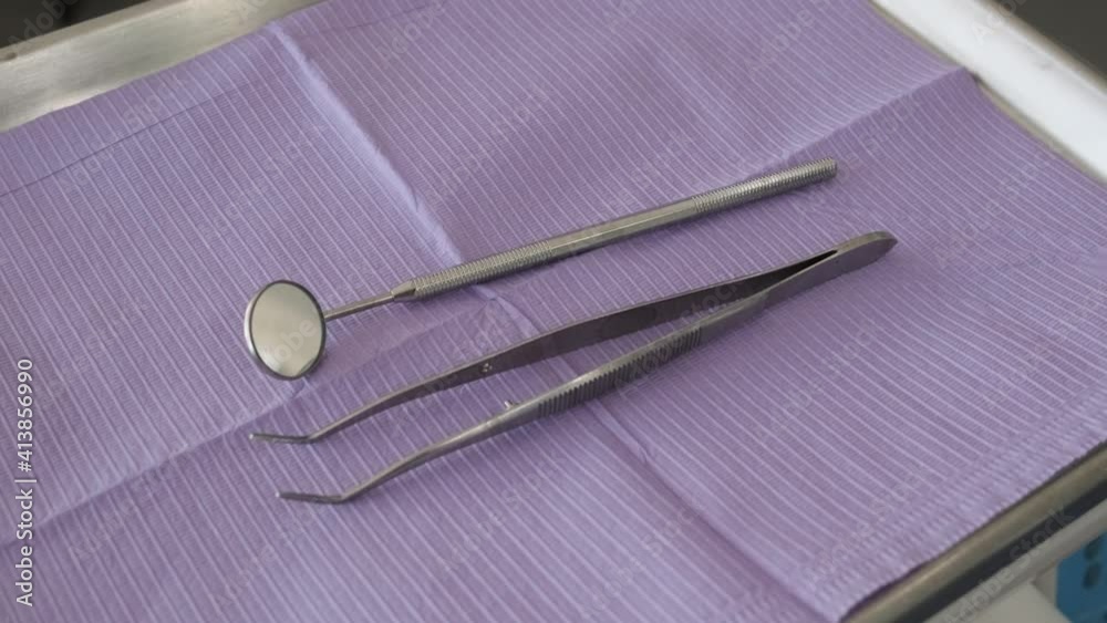 Close-up of a dental tool tray as the dentist places down a mouth mirror and tweezers.