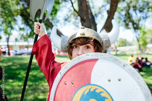 Young teen girl hides her face partially behind viking shield dress up photo