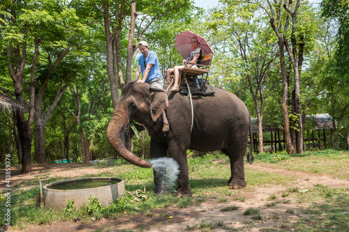 A couple of tourists ride an elephant against the backdrop of the jungle. The elephant washes its feet, pours water on itself