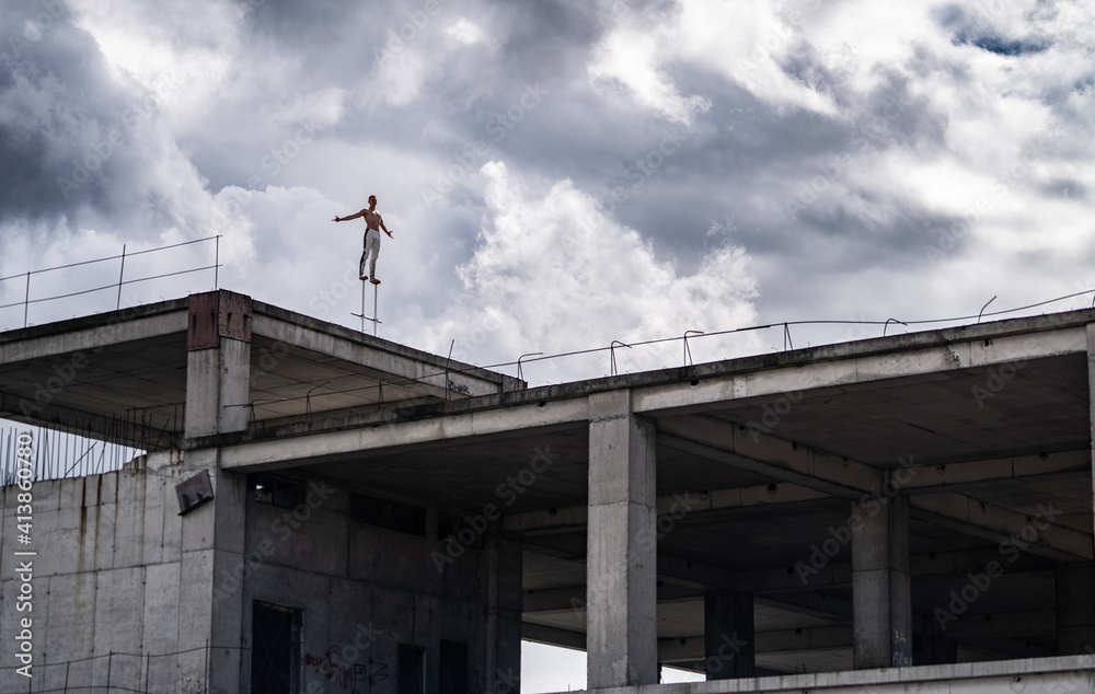 Man standing on the edge of rooftop unfinished building with dramatic clouds on background. Concept of Courage, inspiration and freedom
