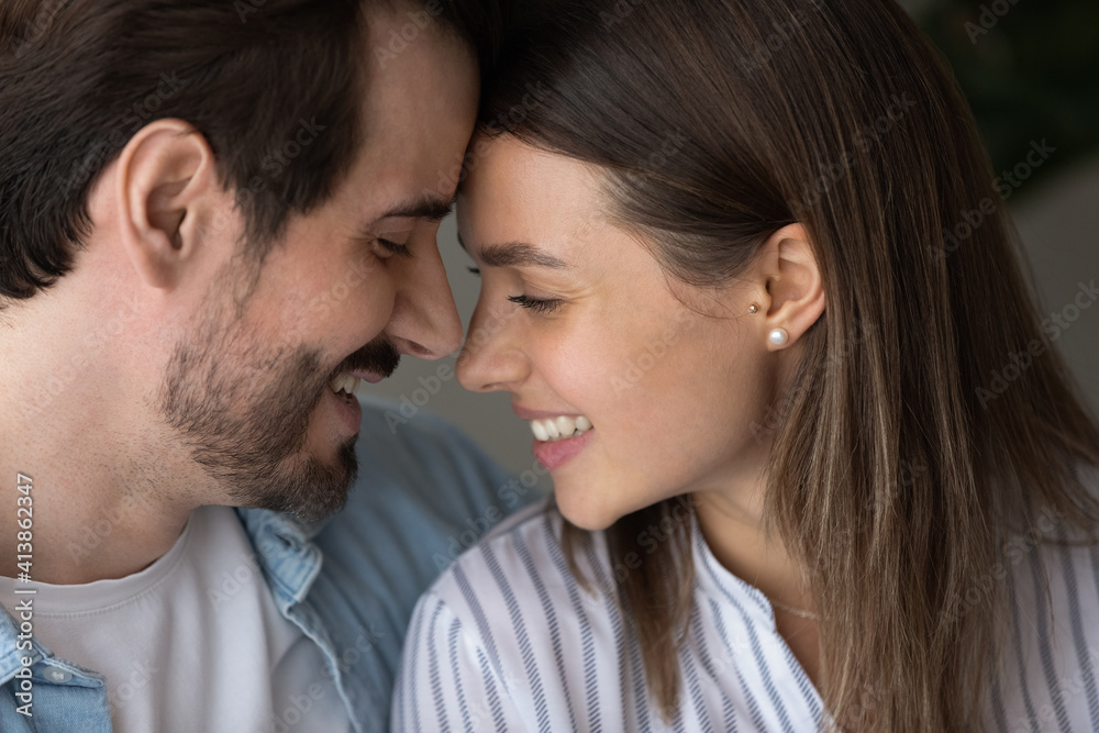 Romantic lovers. Happy young family couple smiling leaning heads close to one another whispering tender sincere confessions. Close up side shot of enamored boyfriend girlfriend faces with closed eyes