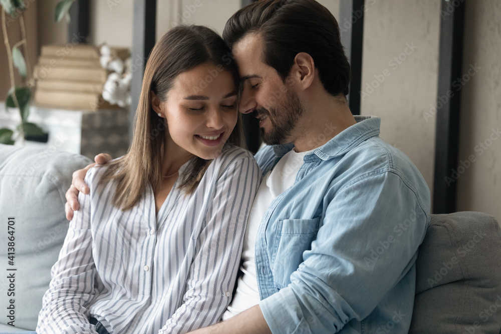 No need in words. Happy serene millennial couple in love embrace on sofa cuddle together sit in silence keep eyes closed. Loving young husband wife relax on soft couch at home enjoy peaceful moment