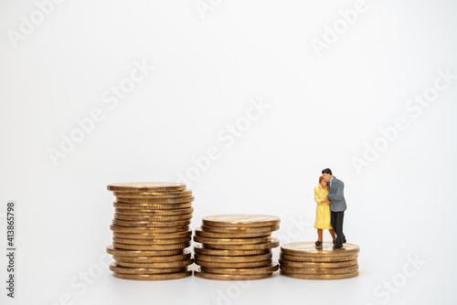 Business, Money, Family and Planning Concept. Businessman and woman miniature figure people hug and walking on unstable stack of gold coins on white background.