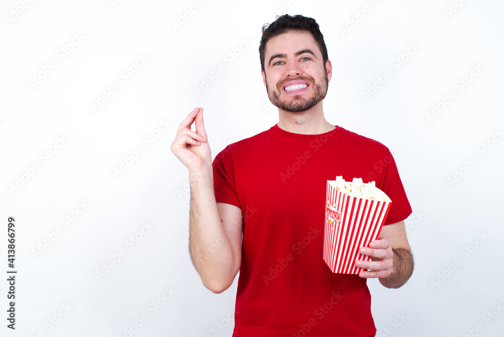 Young handsome man in red T-shirt against white background eating popcorn pointing up with hand showing up seven fingers gesture in Chinese sign language QÄ«. Young handsome man in red T-shirt against white background eating popcorn pointing up with hand showing up seven fingers gesture in Chinese sign language QÄ«.