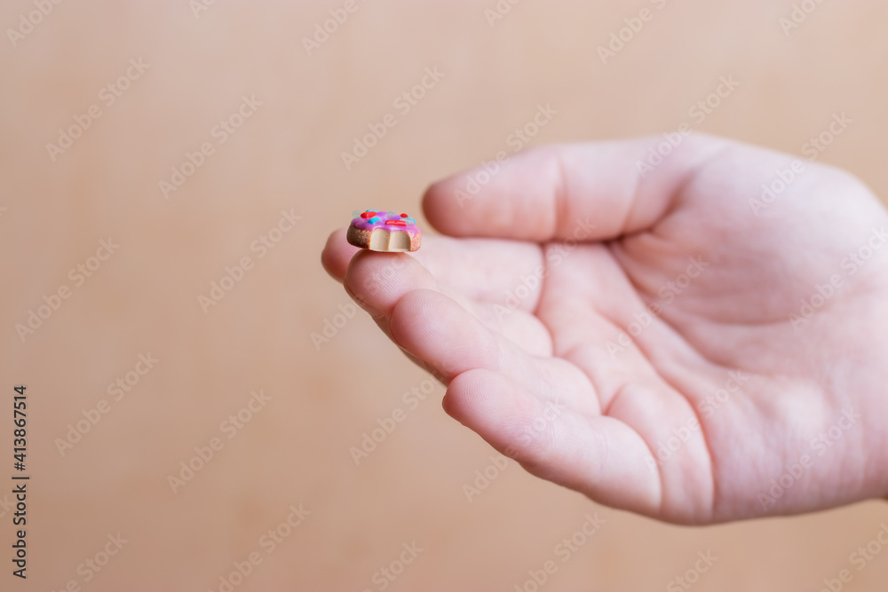 Miniature: donut with polymer clay decor on the fingertips of a woman's hand.