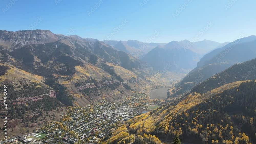 Aerial 4K video of Telluride, Colorado in autumn with beautiful fall colors. Drone clip flying forward between two trees to reveal the picturesque valley and town below.