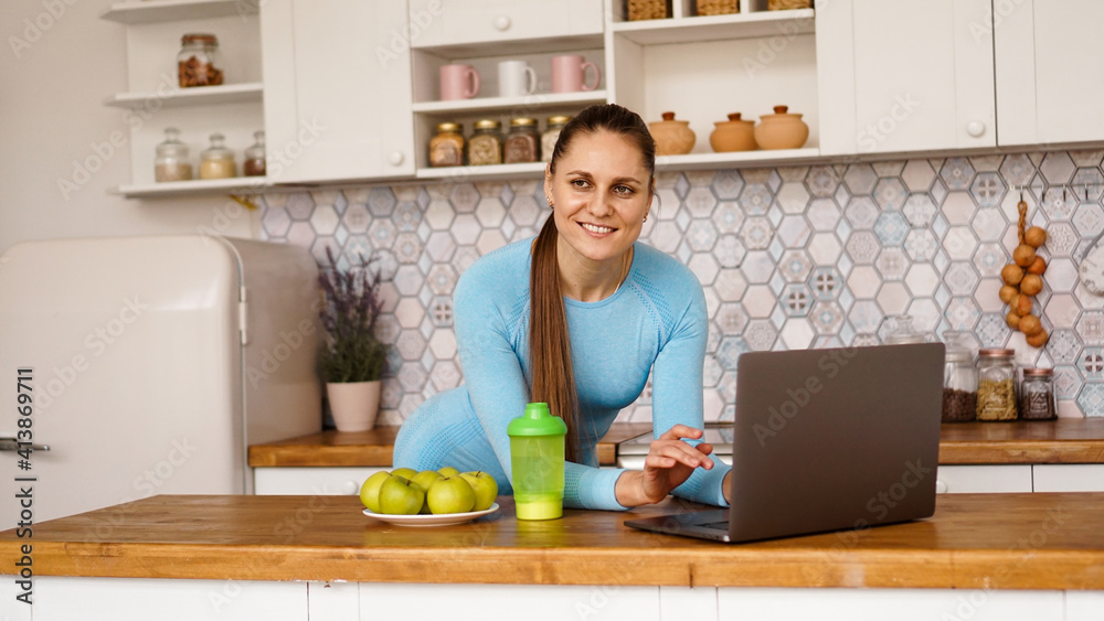 Smiling woman using computer in modern kitchen interior. Cooking and healthy lifestyle concept. A woman is looking at the camera and smiling Smiling woman using computer in modern kitchen interior. Cooking and healthy lifestyle concept. A woman is looking at the camera and smiling