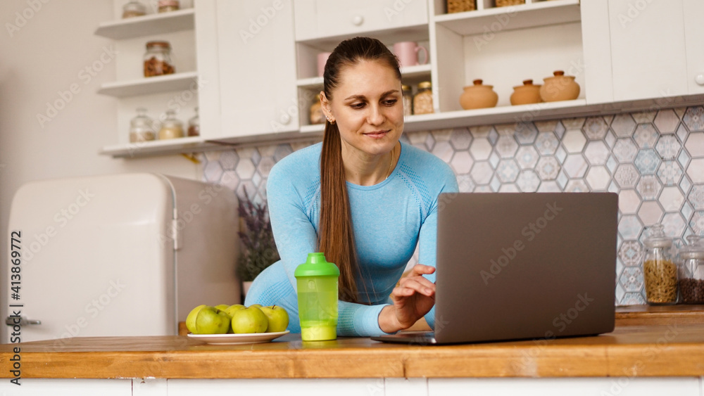 Smiling woman using computer in modern kitchen interior. Cooking and healthy lifestyle concept. A woman is looking for a recipe or is streaming online Smiling woman using computer in modern kitchen interior. Cooking and healthy lifestyle concept. A woman is looking for a recipe or is streaming online