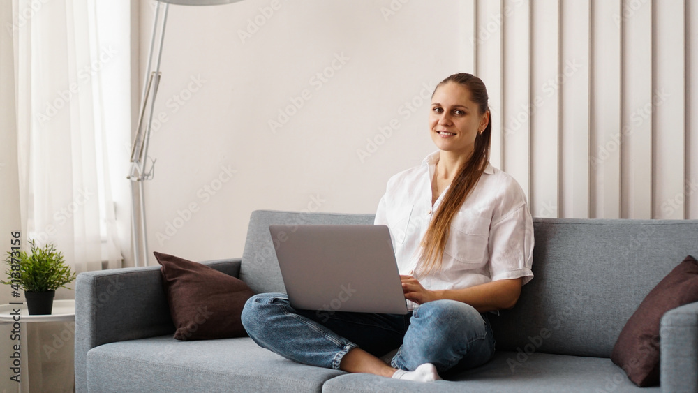 Fototapeta premium Woman working on laptop from home or student studying from home or freelancer. Modern business woman in a white shirt and jeans.