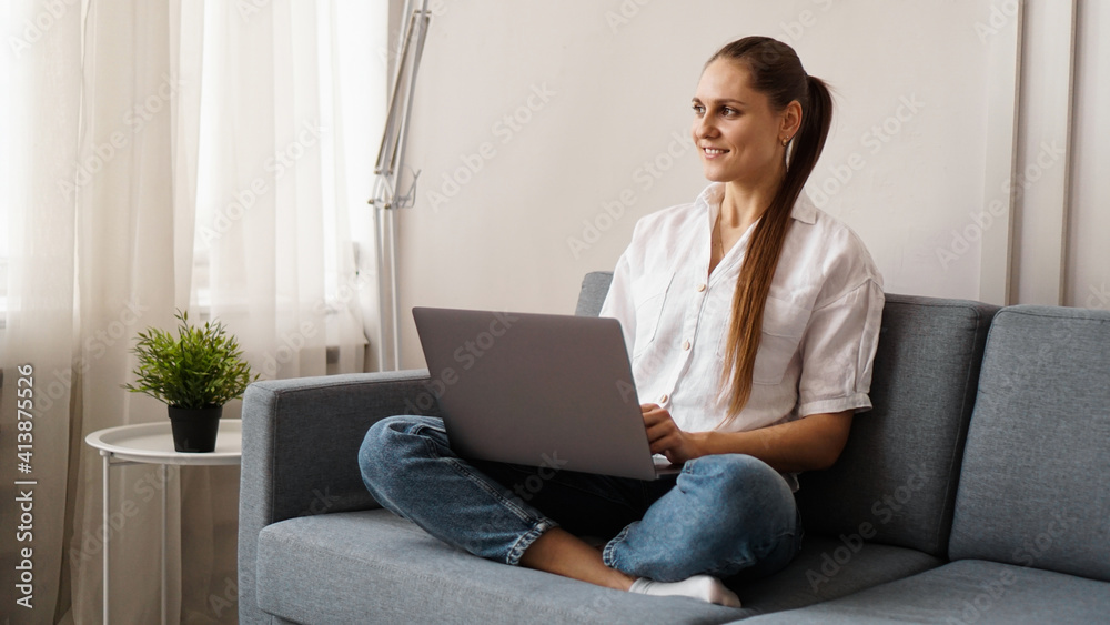 Smiling happy woman sitting on the sofa and using laptop. The concept of remote work or study during quarantine. Smiling happy woman sitting on the sofa and using laptop. The concept of remote work or study during quarantine.