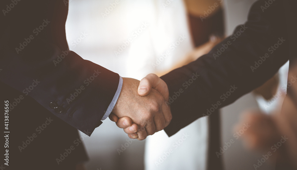 Unknown businesspeople are shaking their hands after signing a contract, while standing together in a sunny modern office, close-up. Business communication, handshake, and marketing concept Unknown businesspeople are shaking their hands after signing a contract, while standing together in a sunny modern office, close-up. Business communication, handshake, and marketing concept