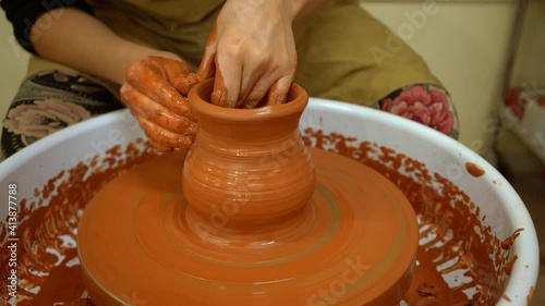 Potter's hands shape a clay jug on a rotating potter's wheel (Close-up). A jug rotates on a potter's wheel. The potter's hands shape the raw orange clay
