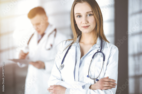 Professional beautiful woman-doctor with a stethoscope is standing straight with crossed arms in a sunny clinic. Young doctors at work in a hospital. Best medicine and healthcare concept