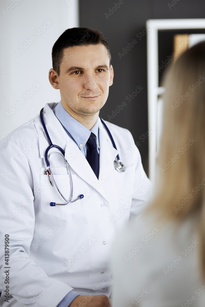 Friendly male doctor and patient woman discussing current health examination while sitting in clinic. Perfect medical service in hospital. Medicine and healthcare concept Friendly male doctor and patient woman discussing current health examination while sitting in clinic. Perfect medical service in hospital. Medicine and healthcare concept