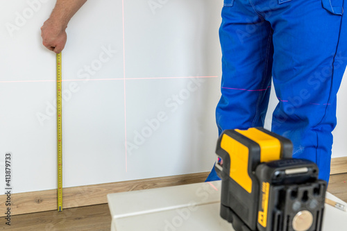 A specialist makes measurements on the wall with a measuring stick and an electronic laser to indicate levels and plumbs