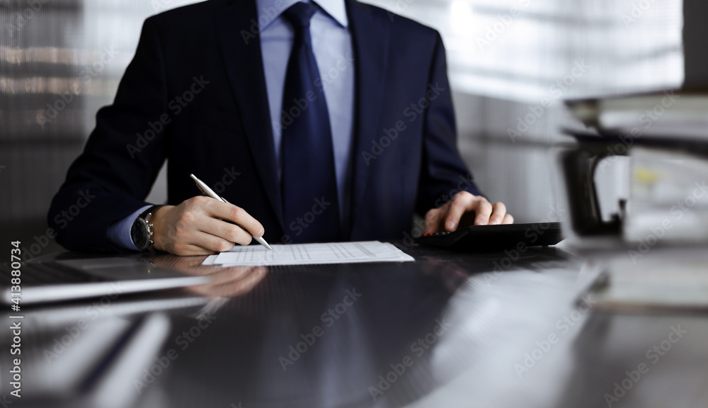 Unknown man accountant in blue blazer use calculator and computer with holding pen on while staying at home during covid pandemic. Taxes and audit concept Unknown man accountant in blue blazer use calculator and computer with holding pen on while staying at home during covid pandemic. Taxes and audit concept