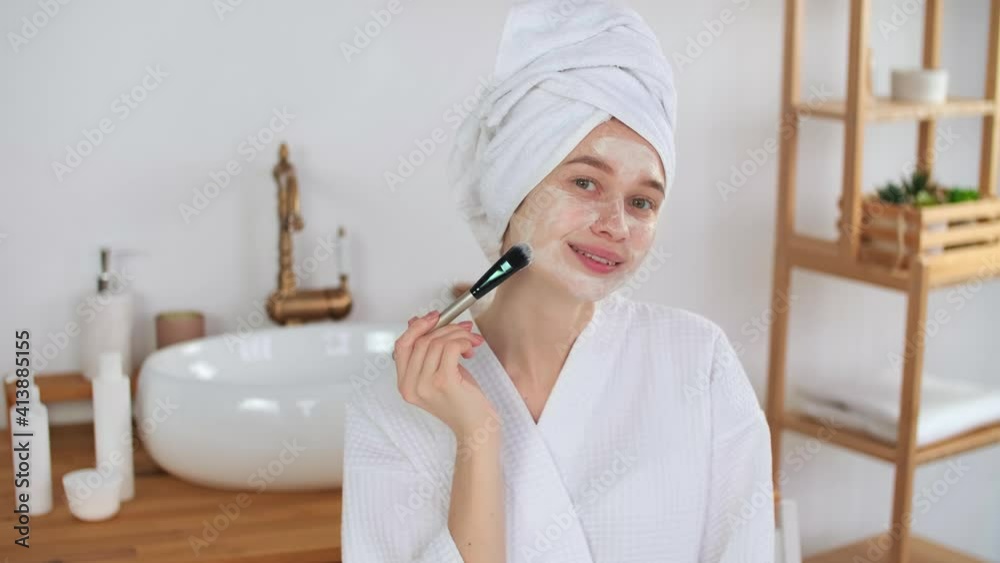 Skin Care, After Bath, Cosmetics at Home, Caucasian Woman, Anti Aging. Caucasian woman in a robe and a towel on her head uses a maxa for the face Skin Care, After Bath, Cosmetics at Home, Caucasian Woman, Anti Aging. Caucasian woman in a robe and a towel on her head uses a maxa for the face