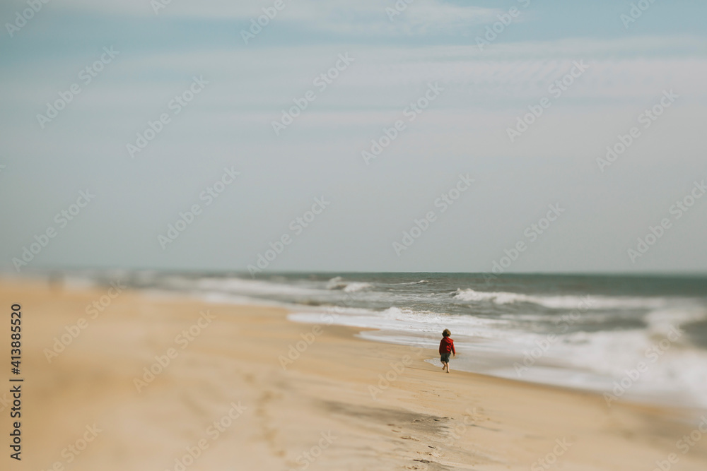 Rear view of boy walking at shore against sky during sunny day