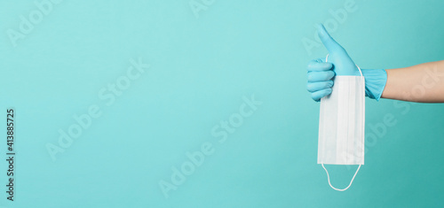 Medical mask on blue and green or Tiffany Blue background.Hand wear surgical glove and holding face mask.and doing like hand sign