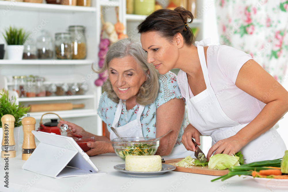 Smiling senior mother and adult daughter cooking together at kitchen Smiling senior mother and adult daughter cooking together at kitchen