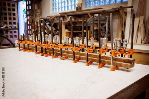 Row bar clamps holding wooden planks on table at workshop photo