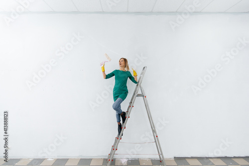 Φωτογραφία A young girl on a stepladder paints a white wall with a roller