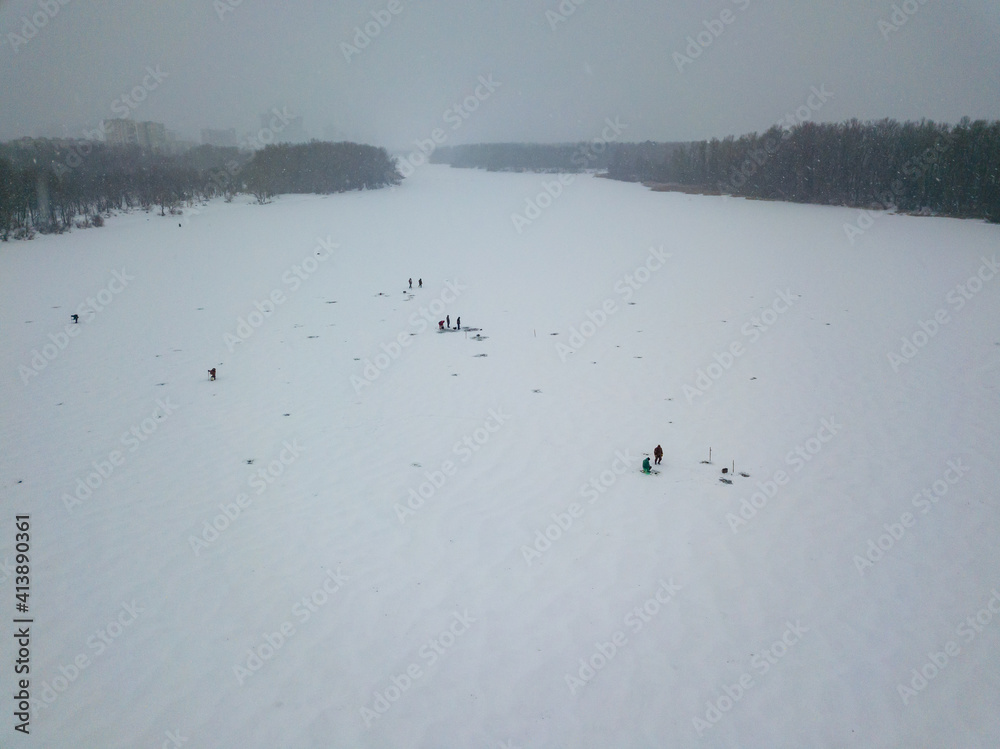 Fishermen on ice in a blizzard. Aerial drone view. Winter snowy morning.