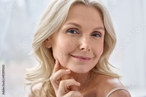 Smiling happy attractive 50s middle aged mature blond woman, old lady looking at camera advertising anti age face skin and body care treatment cosmetics posing in bathroom. Close up headshot portrait