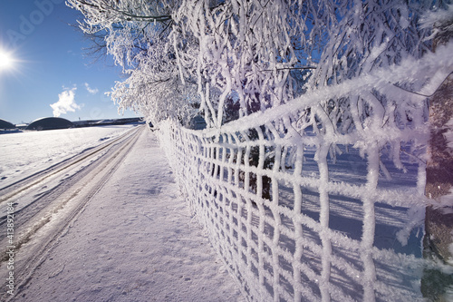 Auf einem ländlichen Feldweg, Zaun und Bäume mit Eiskristallen und Schnee bedeckt, an einem Morgen im Winter