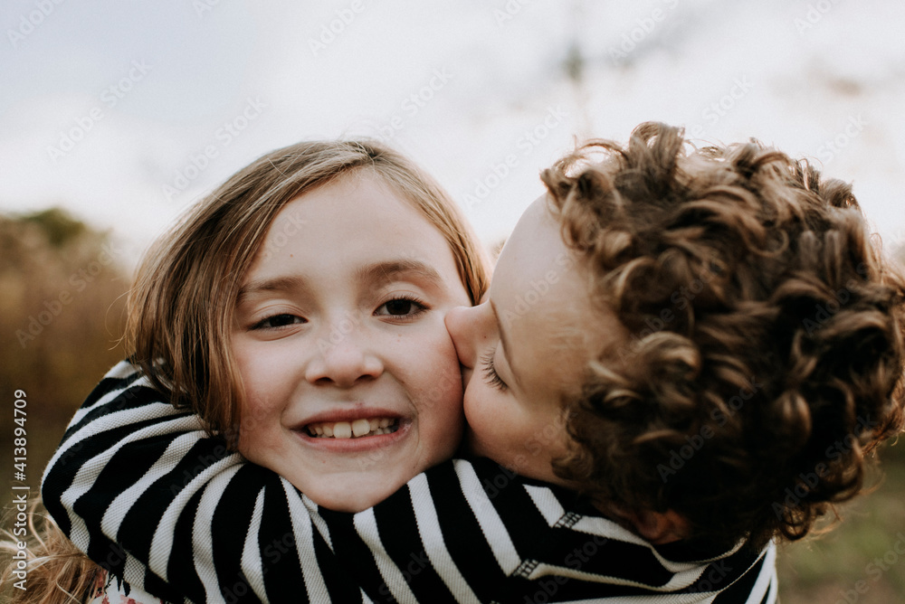 Close-up portrait of smiling sister with loving brother kissing her at park Close-up portrait of smiling sister with loving brother kissing her at park